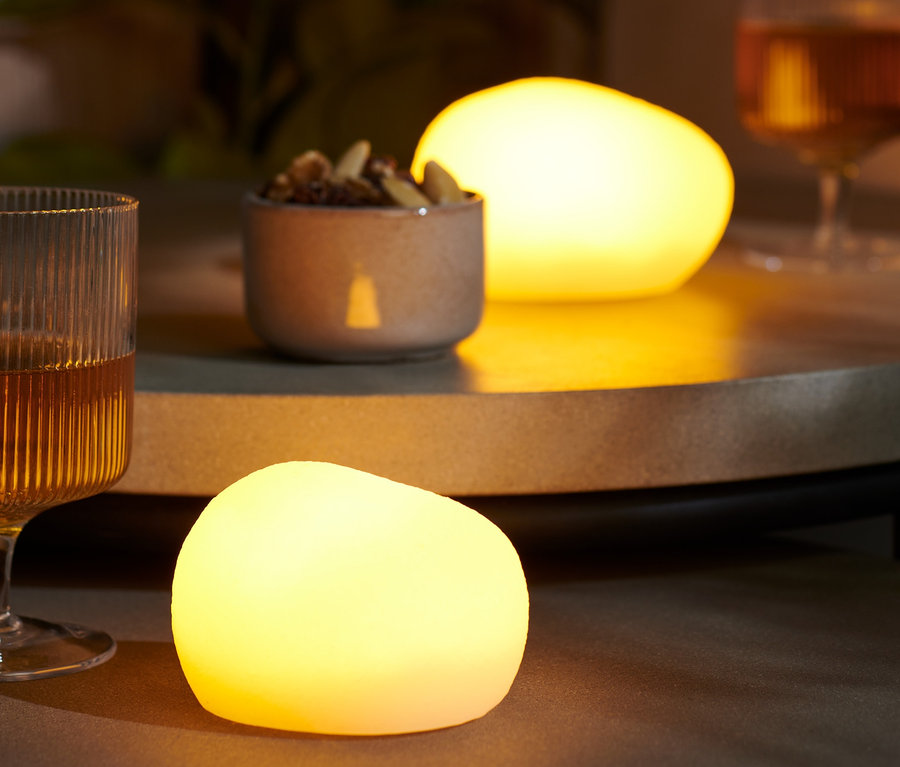 Auf einem Tisch stehen zwei LED-Dekosteine, ein Glas mit einem Getränk und eine Schale Nüsse.