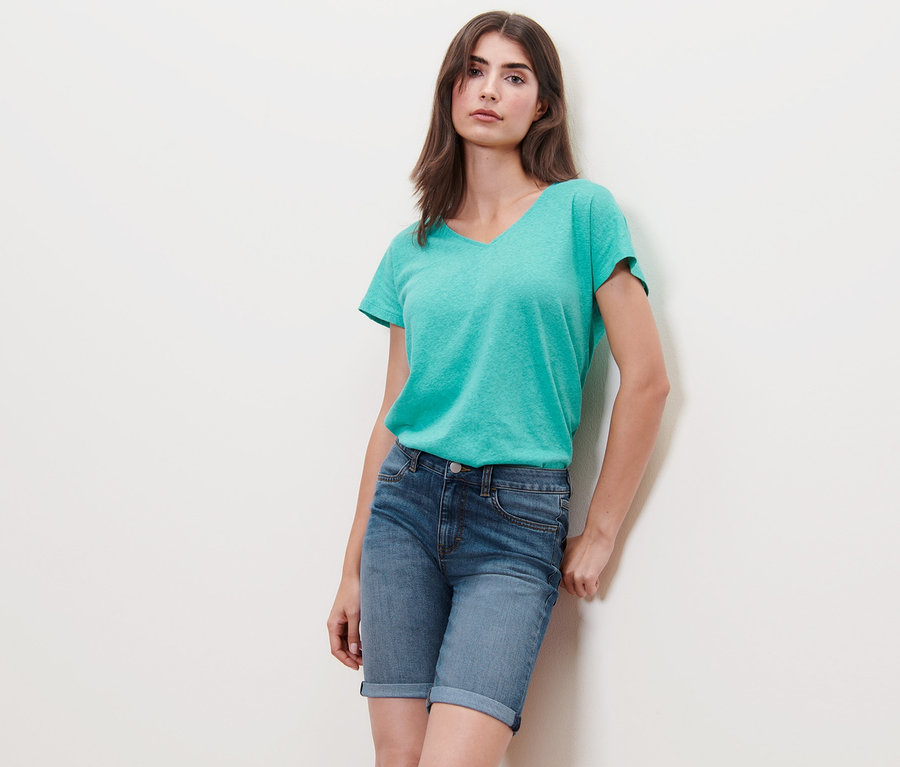 Frau posiert in Denim-Shorts – Fit Lea und einem blaugrünen T-Shirt.
