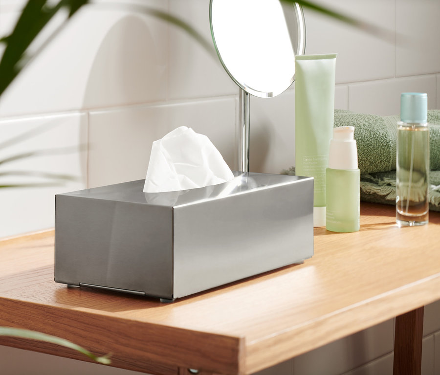 Ein Kosmetiktuchspender aus Metall mit weißen Tüchern auf einem Holzregal.