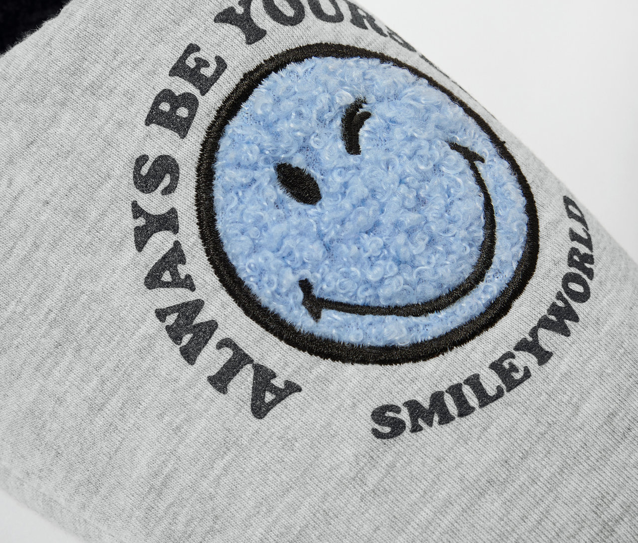 Detailaufnahme eines grauen Hausschuhs von SMILEYWORLD® mit blauem Smiley.