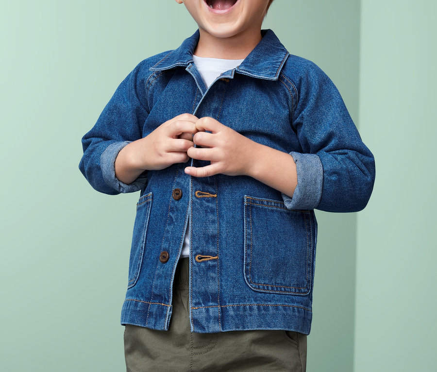Lachender Junge schliesst eine Baumwoll-Denim-Jacke.