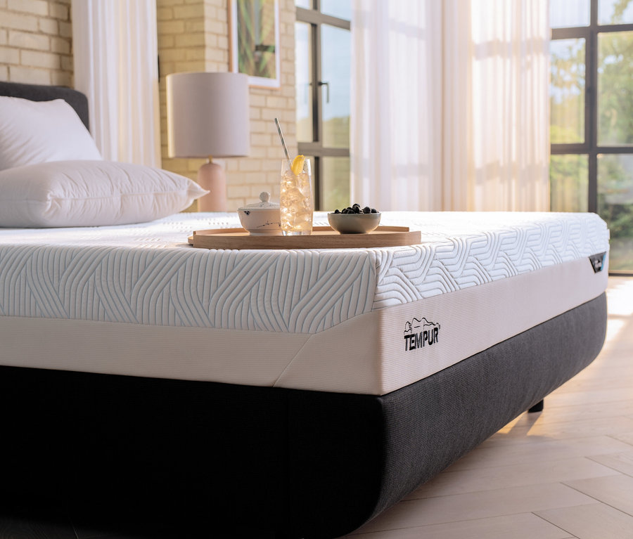 Eine Tempur Matratze Prima, medium, liegt auf einem Bett. Auf der Matratze steht ein Tablett mit einem Getränk und einer Schale mit Obst.