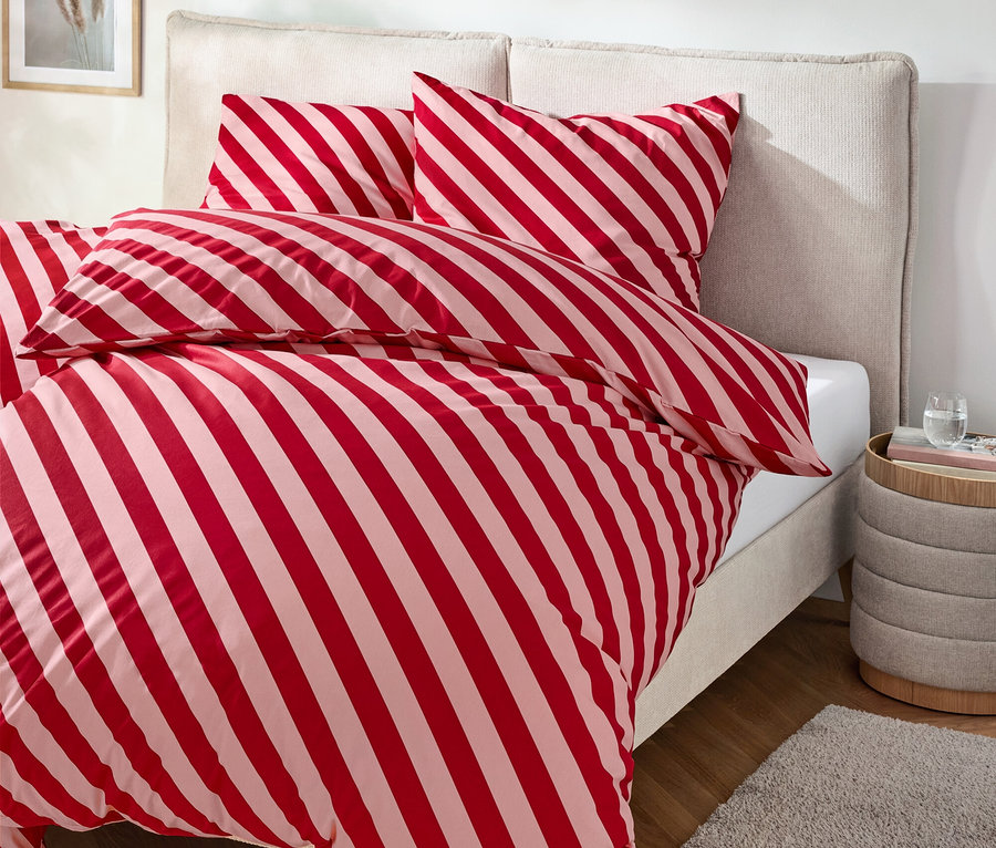 Bett mit rot-weiß gestreifter Bettwäsche, Nachttisch mit Getränk und Teppich.