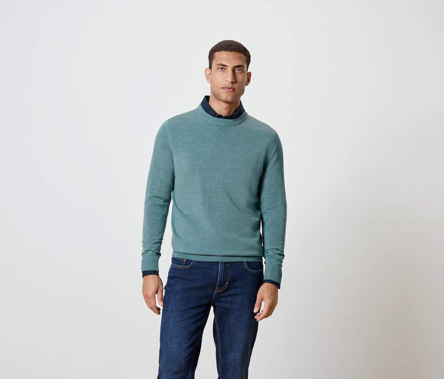 Mann posiert in blauem Pullover und Jeans.