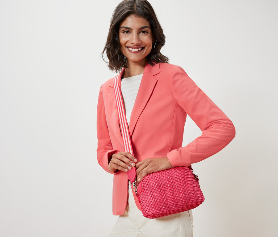 Frau mit rosa Jacke hält eine rosa Umhängetasche.