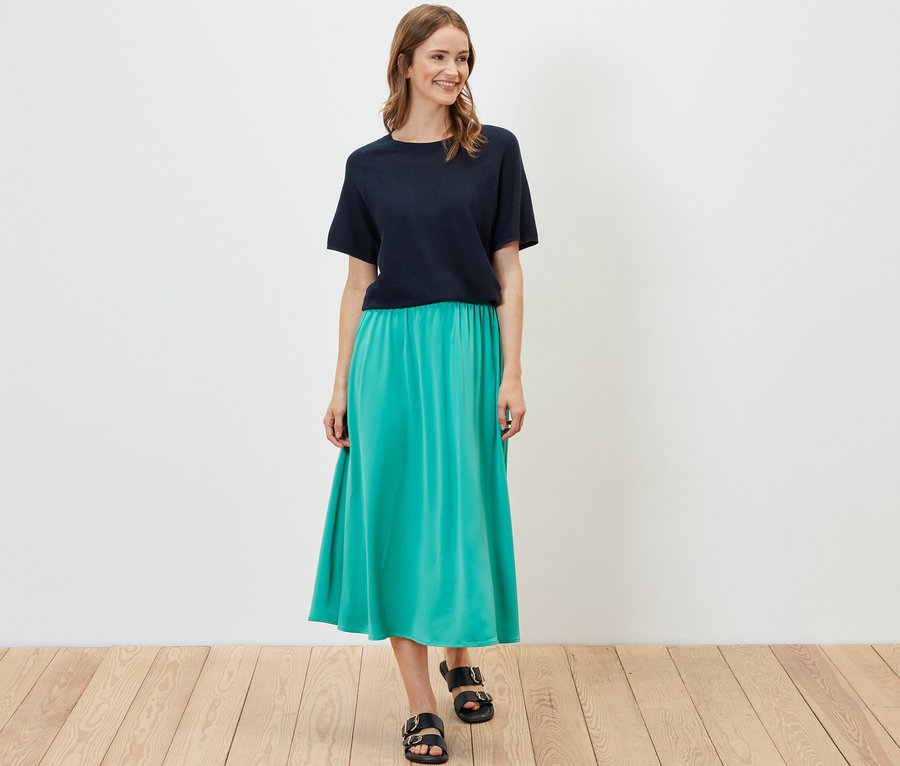 Frau posiert in marineblauem Feinstrick-Shirt und türkisfarbenem Rock.