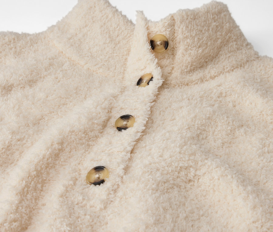 Detailansicht einer cremefarbenen, flauschigen Jacke mit Knöpfen.