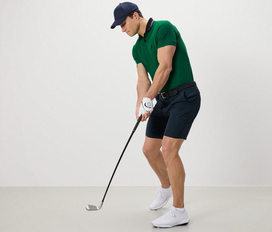 Mann mit grünem Poloshirt und Funktionsshorts beim Golfspielen.