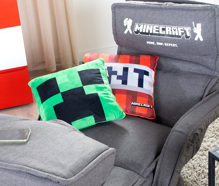 Ein grünes Creeper-Kissen und ein oranges TNT-Kissen liegen auf einem grauen Sessel.
