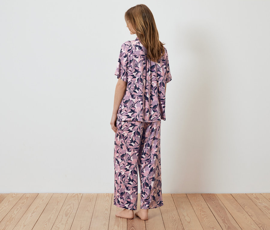 Frau steht mit dem Rücken zur Kamera und trägt einen Pyjama mit Blumenmuster.