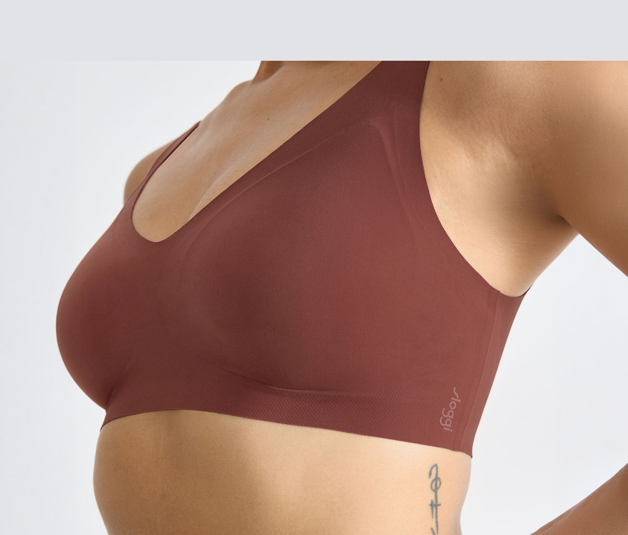 Frau trägt einen braunen sloggi ZERO Feel 2.0 Bralette, von der Seite gesehen, mit einem Tattoo am Rippenbogen.