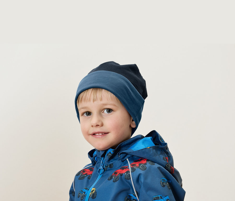 Porträt eines blonden Jungen mit blauer Mütze und Jacke mit Autoaufdruck.