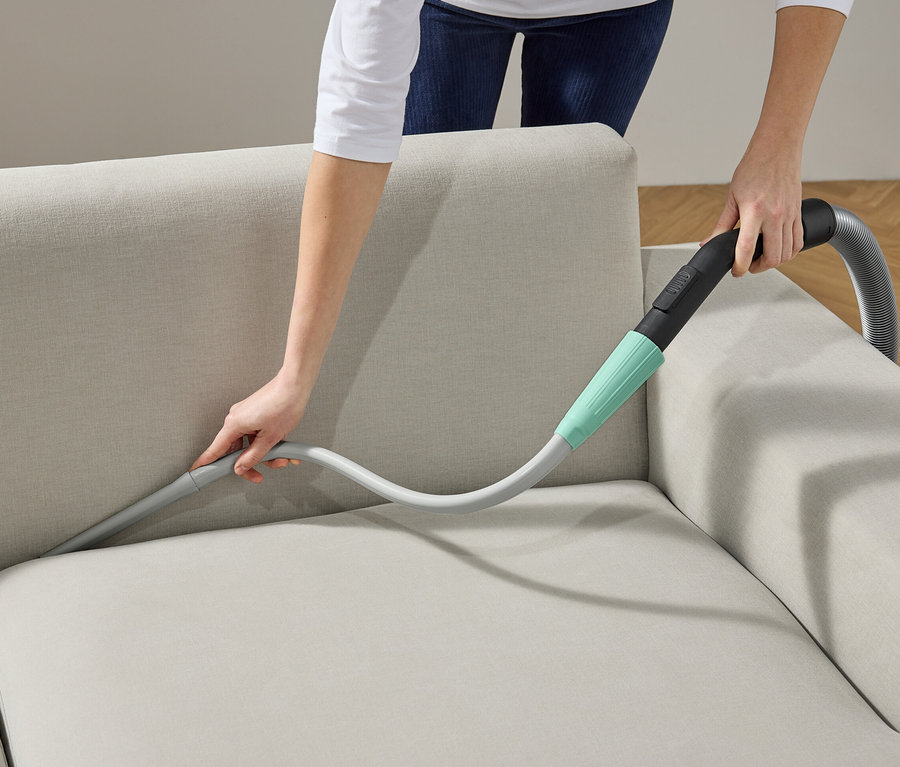 Frau reinigt Sofa mit Staubsauger-Aufsatz.