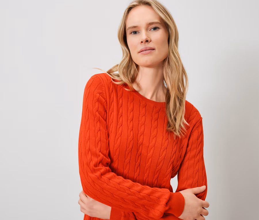 Blonde Frau trägt einen orangefarbenen Pullover.