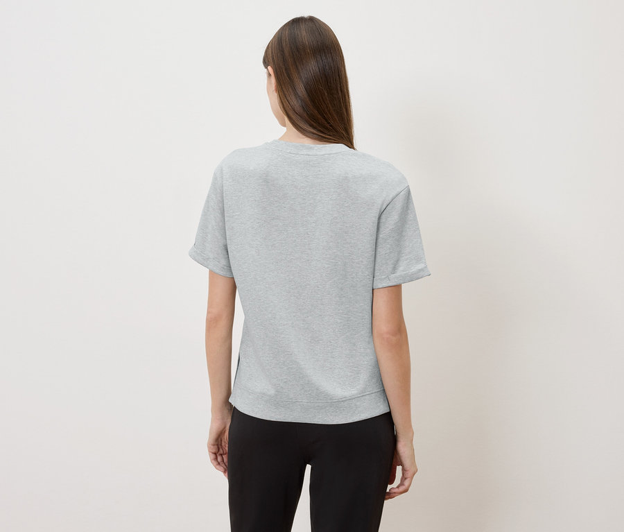 Rückansicht einer Frau mit langen braunen Haaren, die ein graues T-Shirt und eine schwarze Hose trägt.