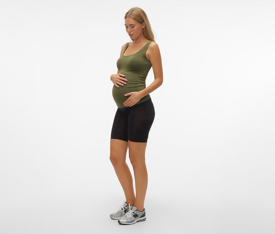 Schwangere Frau mit olivgrünem Top und MAMALICIOUS Skinny Shorts »MLTIA JEANNE«, mellow buff, steht seitlich.
