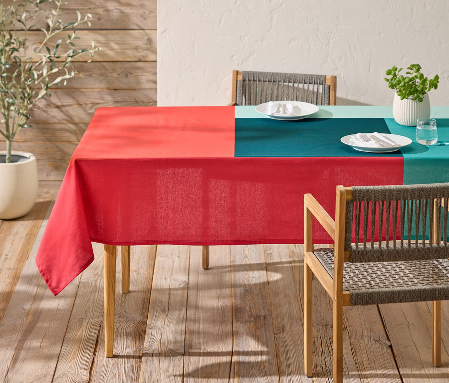 Ein Tisch mit einer rot und blaugrün karierten Tischdecke und zwei Stühlen steht auf einer Holzterrasse.