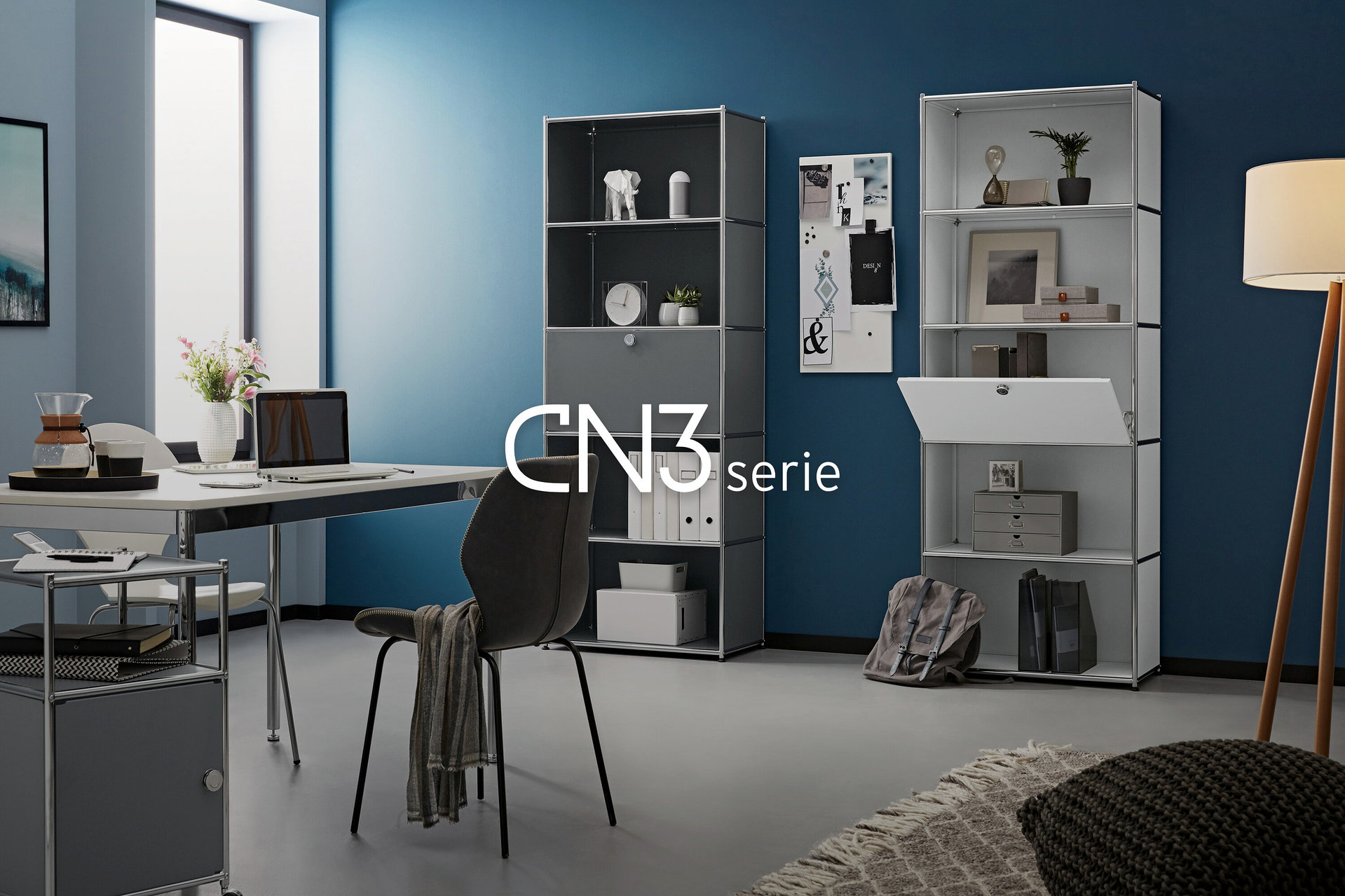 Ein Arbeitszimmer mit zwei grauen und weißen Regalen, einem Schreibtisch mit Laptop und einer Lampe.