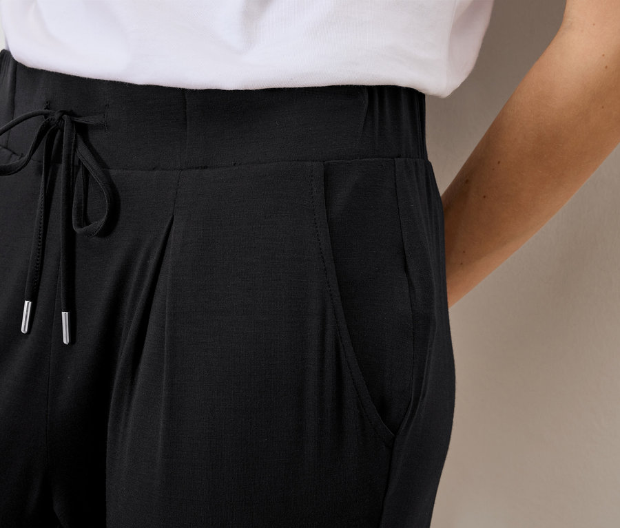 Nahaufnahme einer Frau, die eine locker sitzende, schwarze Hose mit Kordelzug und Taschen trägt.