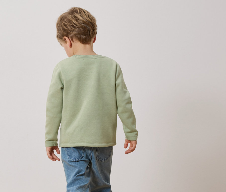 Ein Kind von hinten, trägt einen hellgrünen Pullover und Jeans.