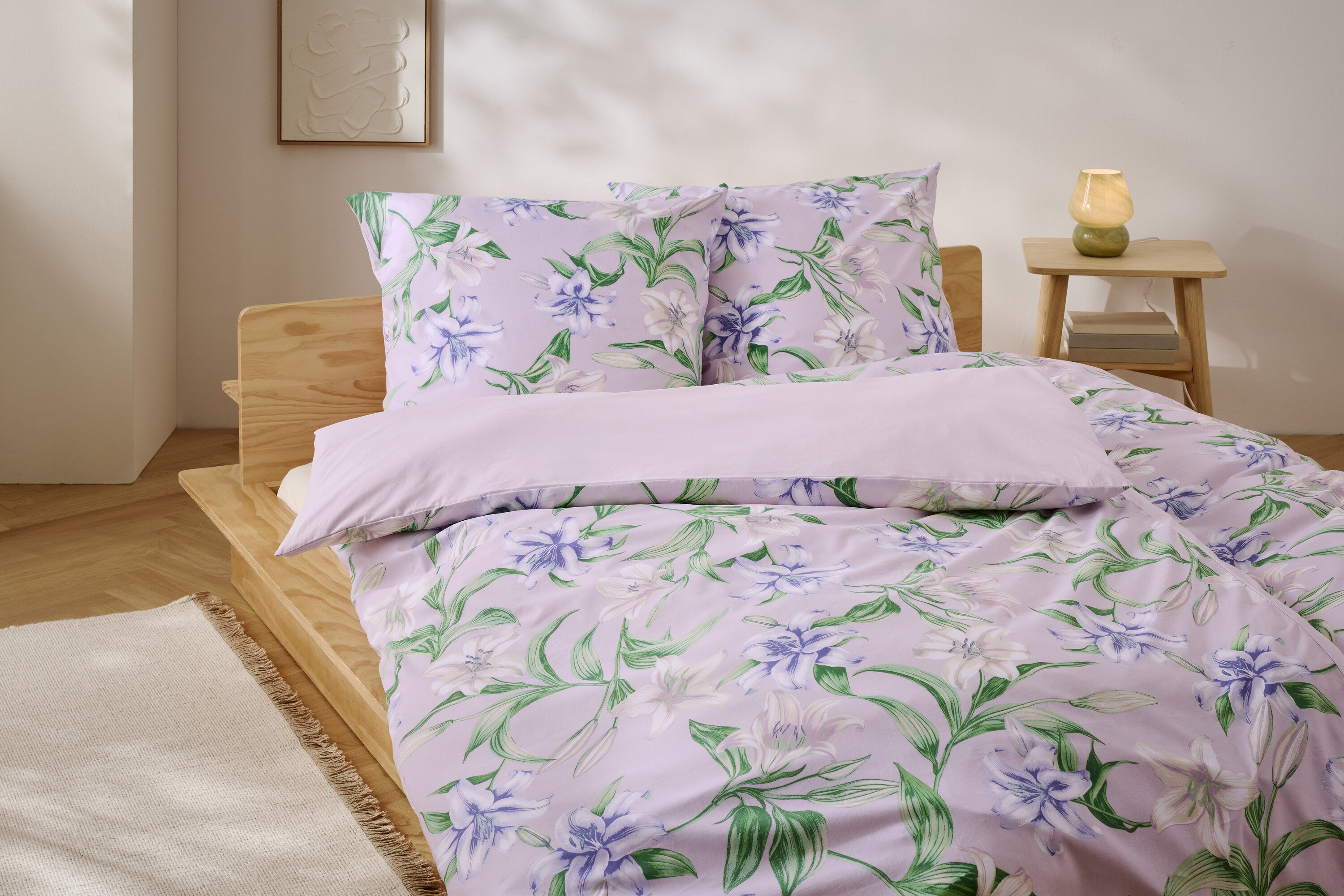 Bett mit lila Bettwäsche mit Blumenmuster und Holzrahmen.