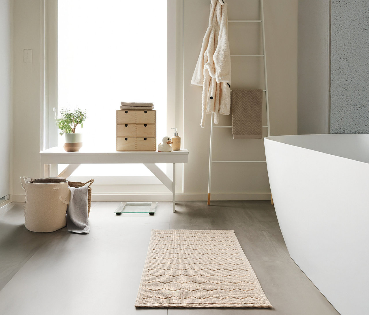 Ein Badezimmer mit einer beigen benuta Badematte »Jojo« mit Rautenmuster, Größe 50 x 80 cm, vor einer weißen Badewanne.