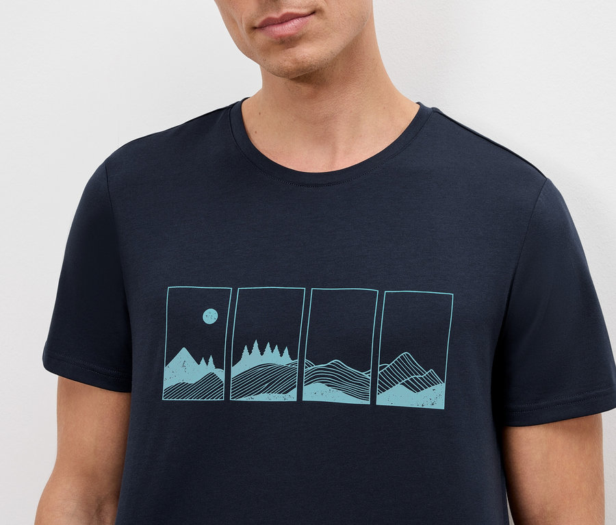 Nahaufnahme eines Mannes, der ein marineblaues T-Shirt mit einem Berglandschafts-Design trägt.