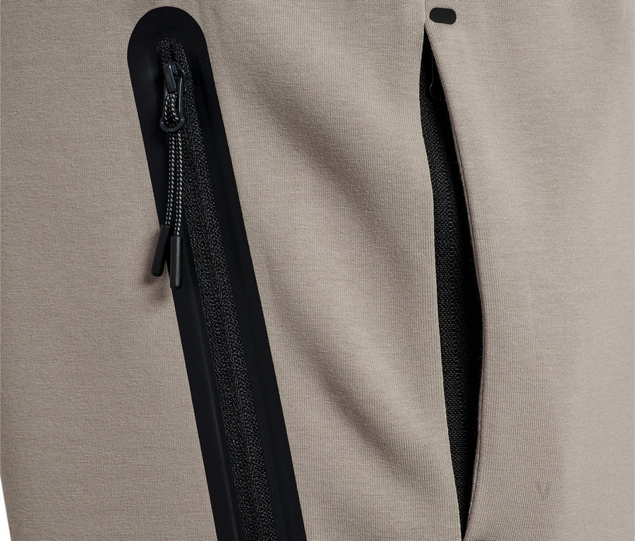Nahaufnahme von beigen Trainingshosen mit einer schwarzen Reißverschlusstasche und einer offenen Tasche.