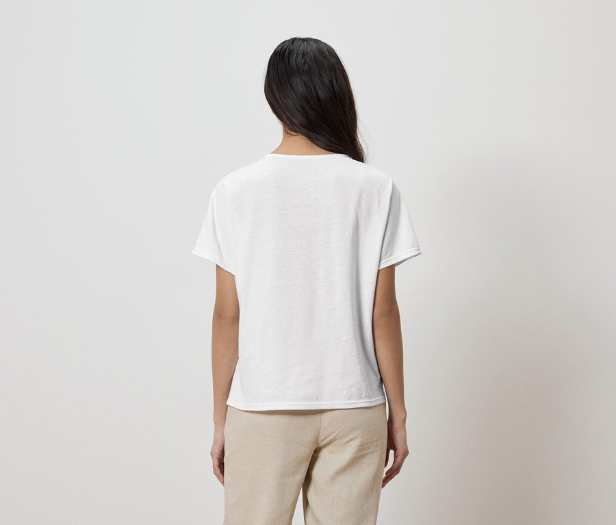 Rückenansicht einer Frau mit langen dunklen Haaren, die ein weißes T-Shirt und beigefarbene Hosen trägt.