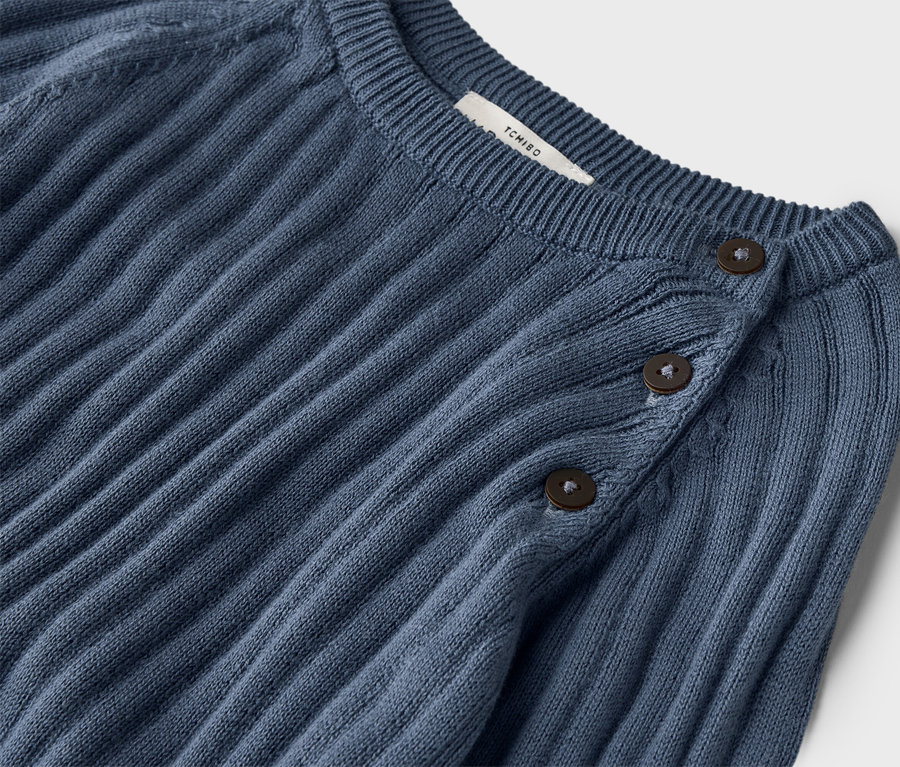 Nahaufnahme eines gerippten, dunkelblauen Strickpullovers mit drei Knöpfen am Kragen.