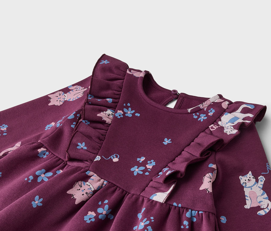 Dunkelviolettes Kinderkleid mit Rüschen an den Schultern und einem Muster aus rosa und blauen Katzen sowie kleinen blauen Blumen.