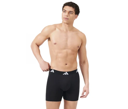 Oberkörperfreier Mann trägt schwarze Boxershorts mit weißem adidas Logo-Bund, blickt nach rechts und hält die linke Hand am Bund.