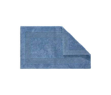 Ein rechteckiger, blauer Badteppich mit strukturiertem Rand, dessen obere rechte Ecke umgeschlagen ist.