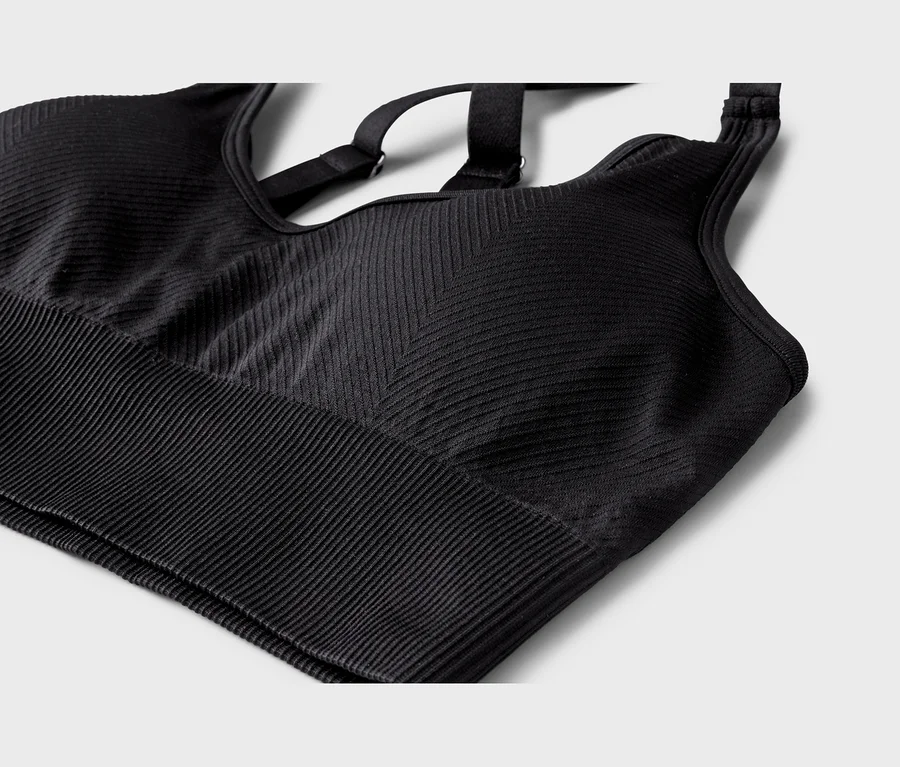Schwarzer Sport-BH aus geripptem Stoff, mit horizontalen Rippen am Bund und einem Chevron-Muster am Hauptteil. Verstellbare Kreuzträger sind sichtbar.