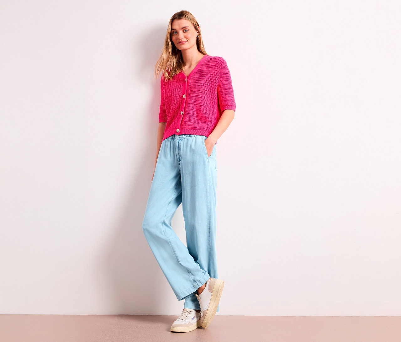 Blonde Frau trägt eine pinkfarbene Strickjacke und eine hellblaue, weite Street One Jeans »Emee«.