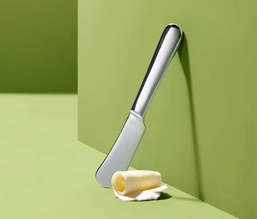 Ein Buttermesser und eine Butterrolle auf grünem Hintergrund.