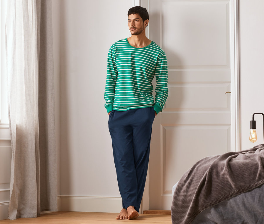 Mann steht im Schlafzimmer und trägt einen gestreiften Jersey-Pyjama.