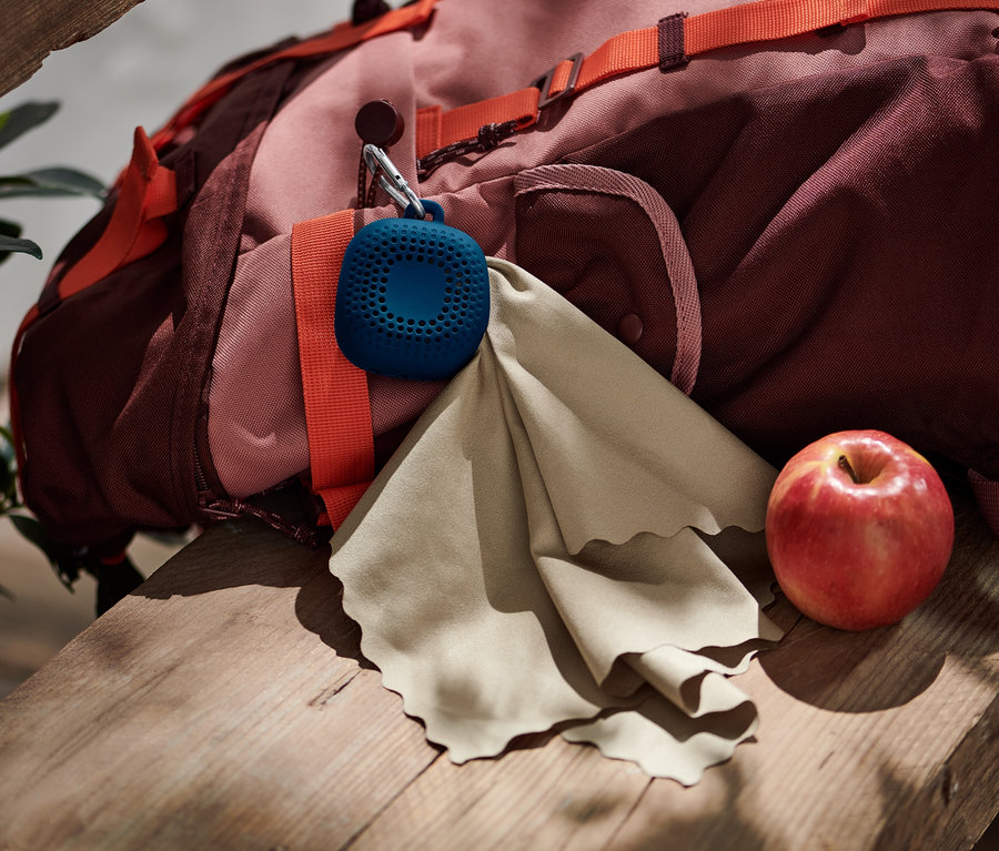 Ein Rucksack, ein Outdoor-Handtuch und ein Apfel liegen auf einer Holzbank.