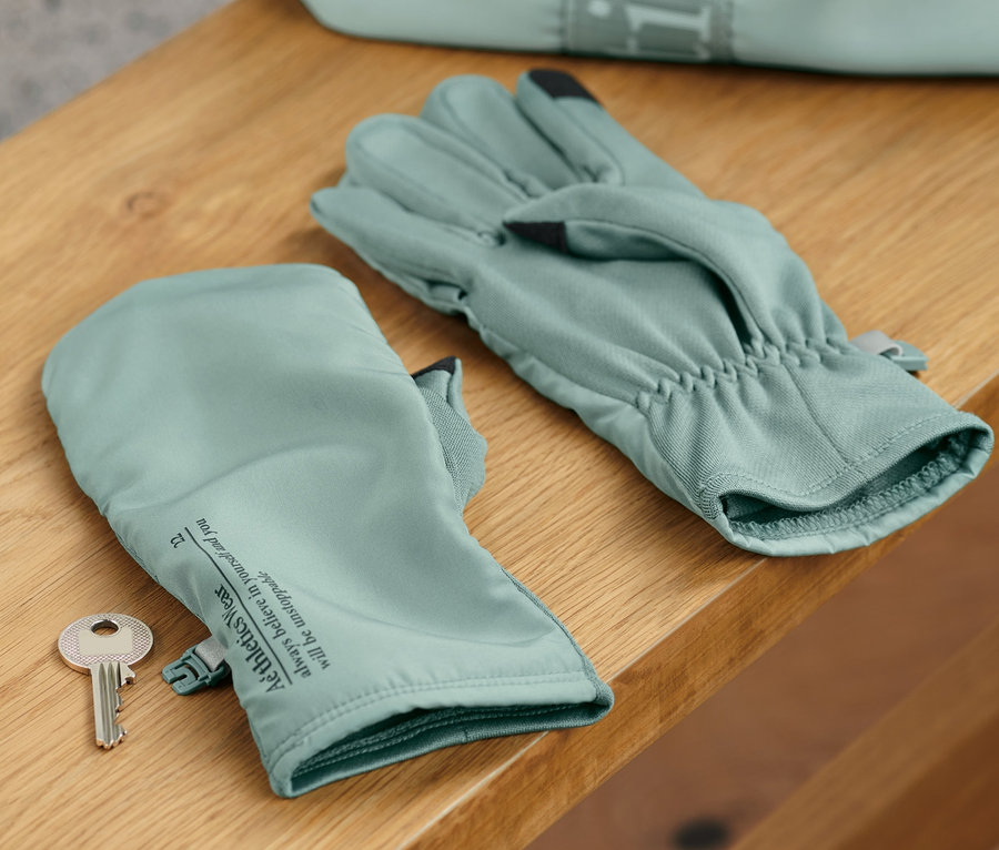 Auf einem Holzregal liegen Klapp-Laufhandschuhe und ein Schlüssel, im Hintergrund eine Tasche.