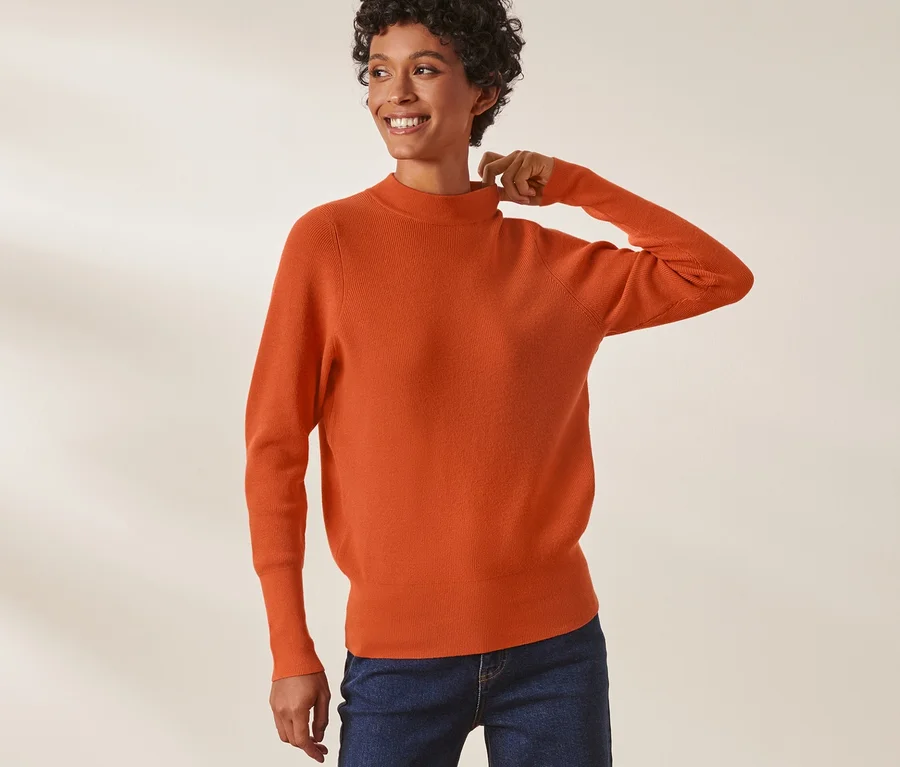 Frau posiert in Strickpullover und Jeans.