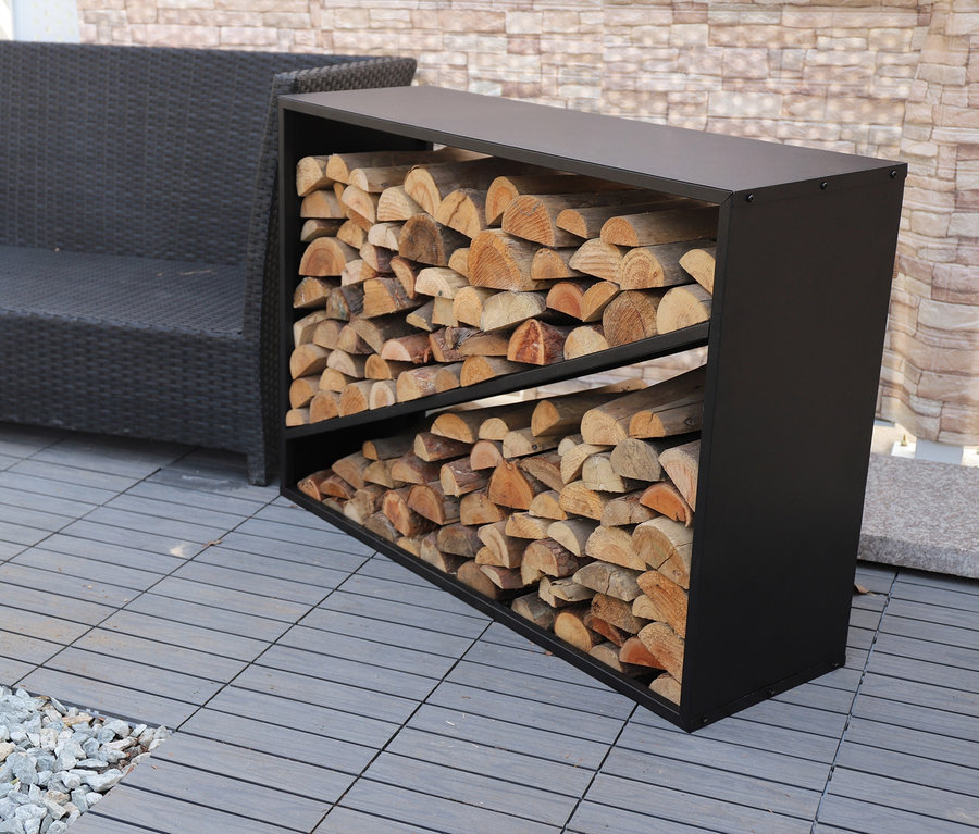 Ein ca. 114 cm großes Kaminholzregal gefüllt mit Holzscheiten steht draußen neben einem grauen Sofa.