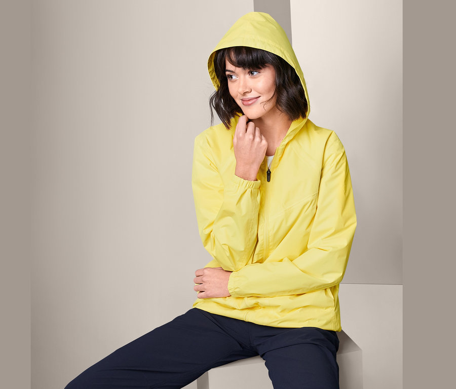 Frau sitzt und trägt eine gelbe Lightweight-Regenjacke »pack me«.