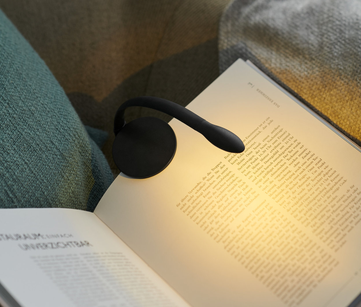 Schwarze LED-Leseleuchte ist an einem offenen Buch auf einem Sessel befestigt.