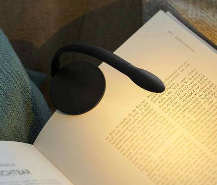 Schwarze LED-Leseleuchte ist an einem offenen Buch auf einem Sessel befestigt.