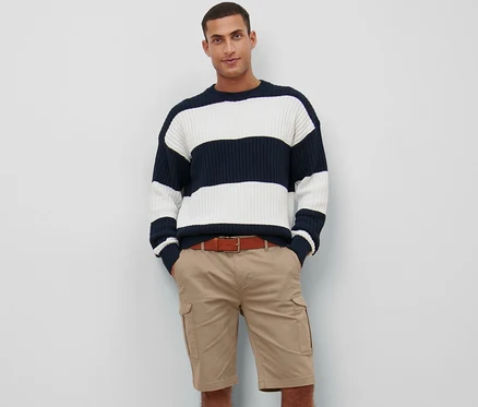 Mann posiert in beigen Cargo-Shorts und einem marineblau-weiß gestreiften Pullover.