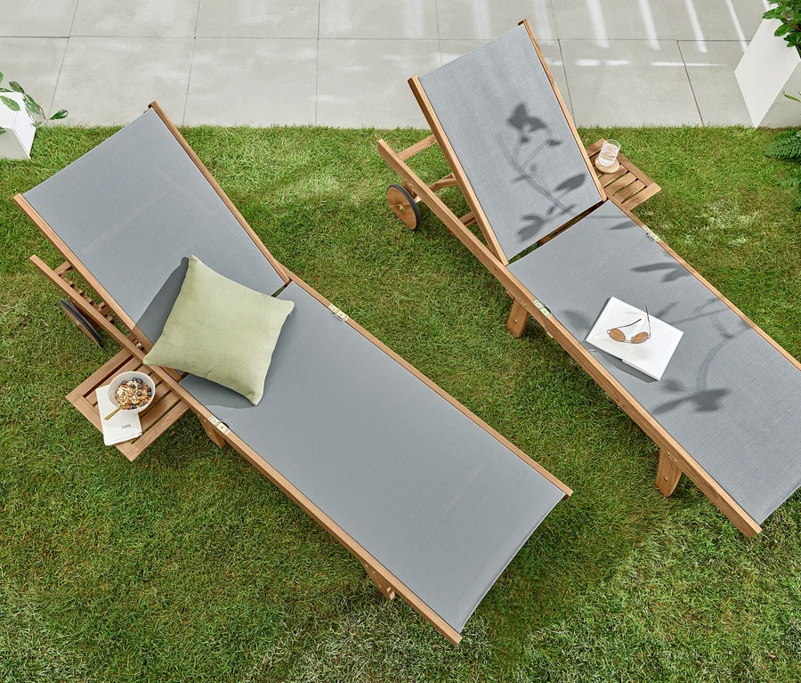 Zwei Liegen »Lenja« mit ausziehbarem Tabletttisch auf einer Wiese. Auf einer Liege liegen ein Buch und eine Sonnenbrille.
