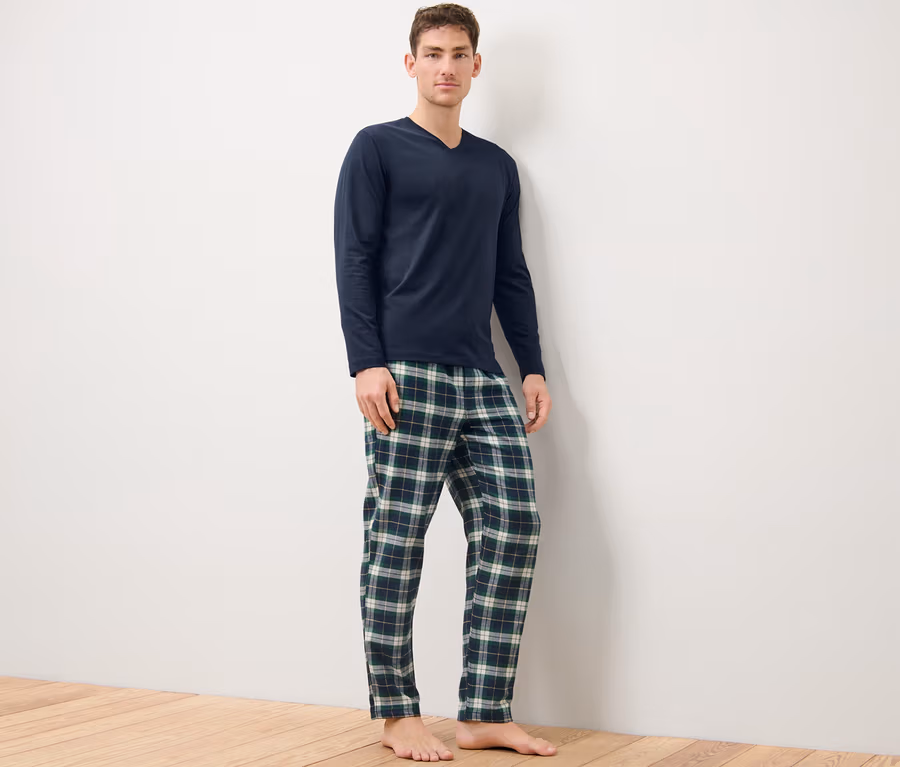 Mann steht und trägt einen blau-grünen Flanellpyjama.