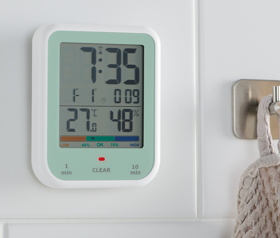 Eine digitale Uhr mit Hygro- und Thermometer hängt an einer weißen Wand. Das Display zeigt 7:35 Uhr, 27 Grad und 48% Luftfeuchtigkeit.