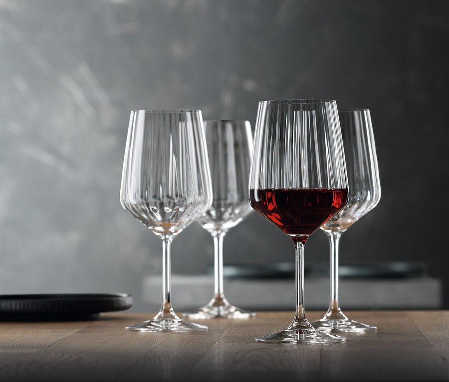 Vier Spiegelau Rotweingläser »Lifestyle« aus einem 8er-Set stehen auf einem Tisch, eines davon ist mit Rotwein gefüllt.