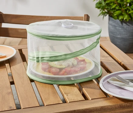 Eine faltbare Mini-Abdeckhaube steht auf einem Holztisch und schützt einen Teller mit Essen.